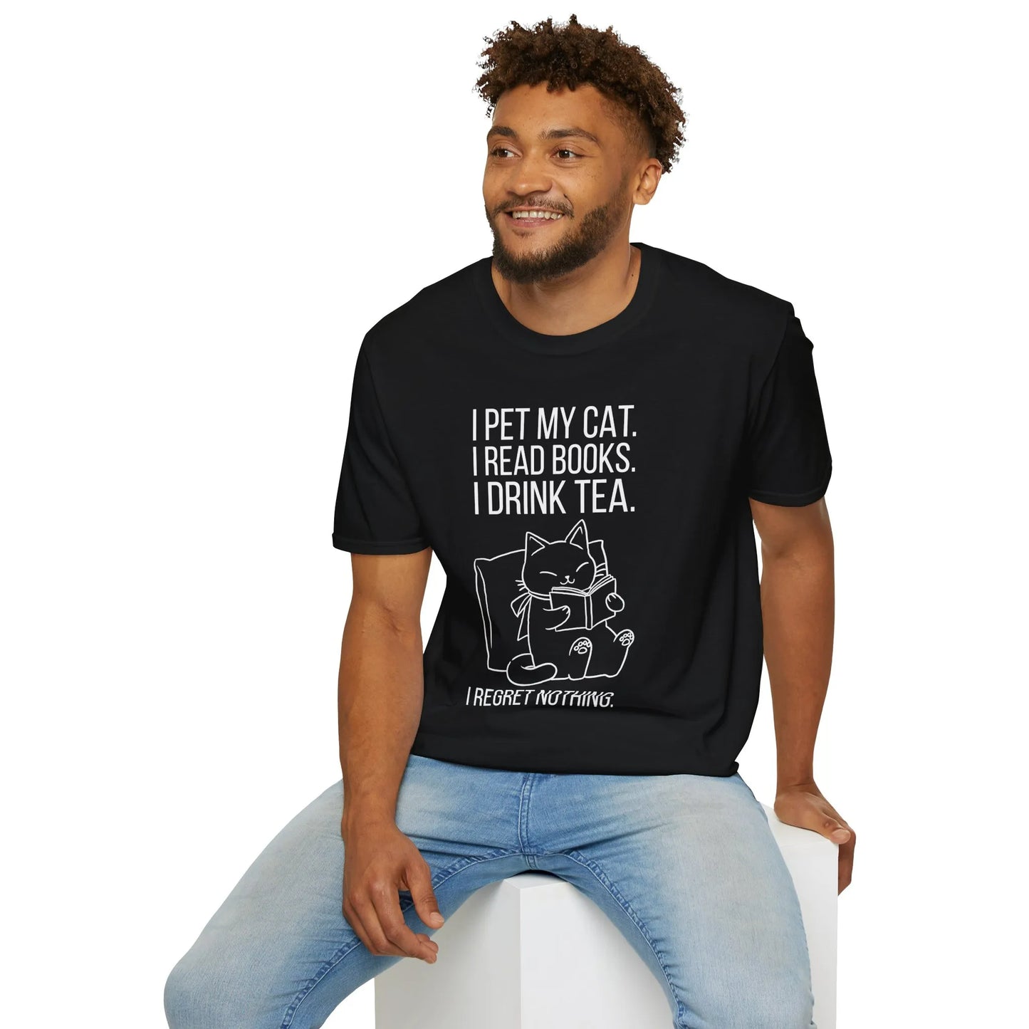 Cozy scene of a man in a book nook wearing a Purrfect Tea & Tales T-Shirt, enjoying tea, cat by his side, embracing a reading lifestyle.