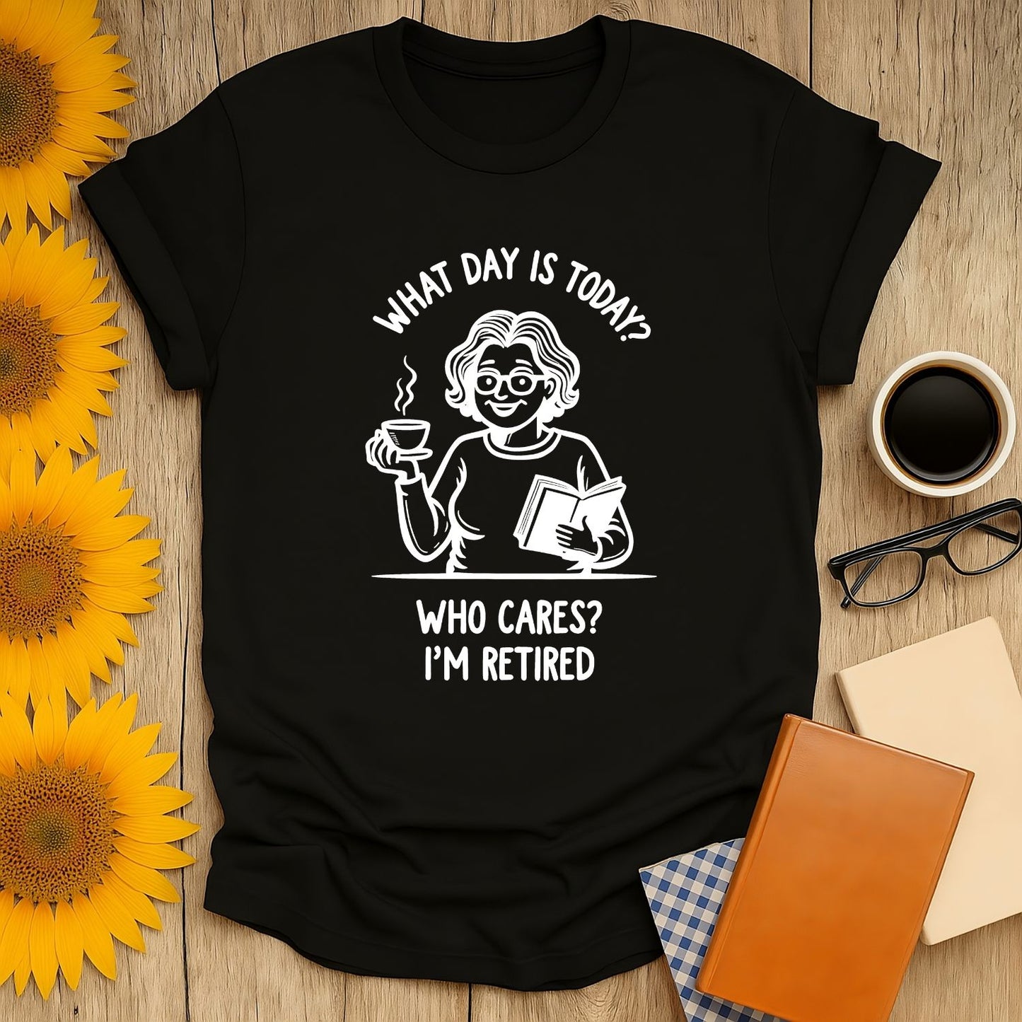 Black t-shirt with humorous design 'What day is today? Who cares? I'm retired' featuring a smiling woman with coffee and a book.