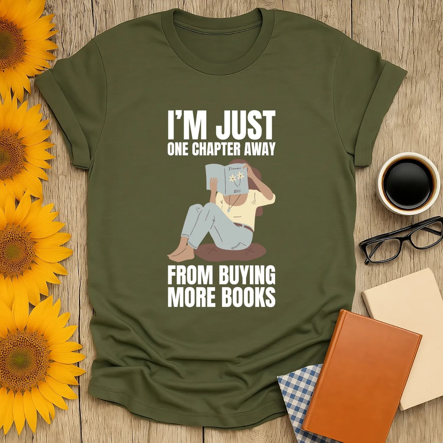 Book lover shirt featuring a cozy illustration of a person reading, saying "I'M JUST ONE CHAPTER AWAY FROM BUYING MORE BOOKS".