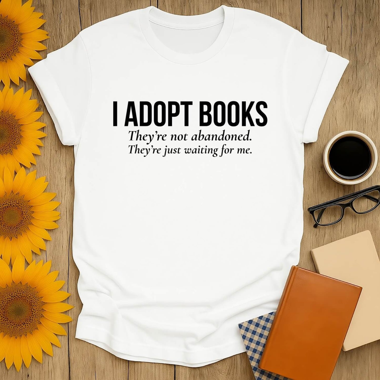 Book lover t-shirt featuring 'I Adopt Books' message, perfect for reading enthusiasts, on a flat lay with flowers and books.