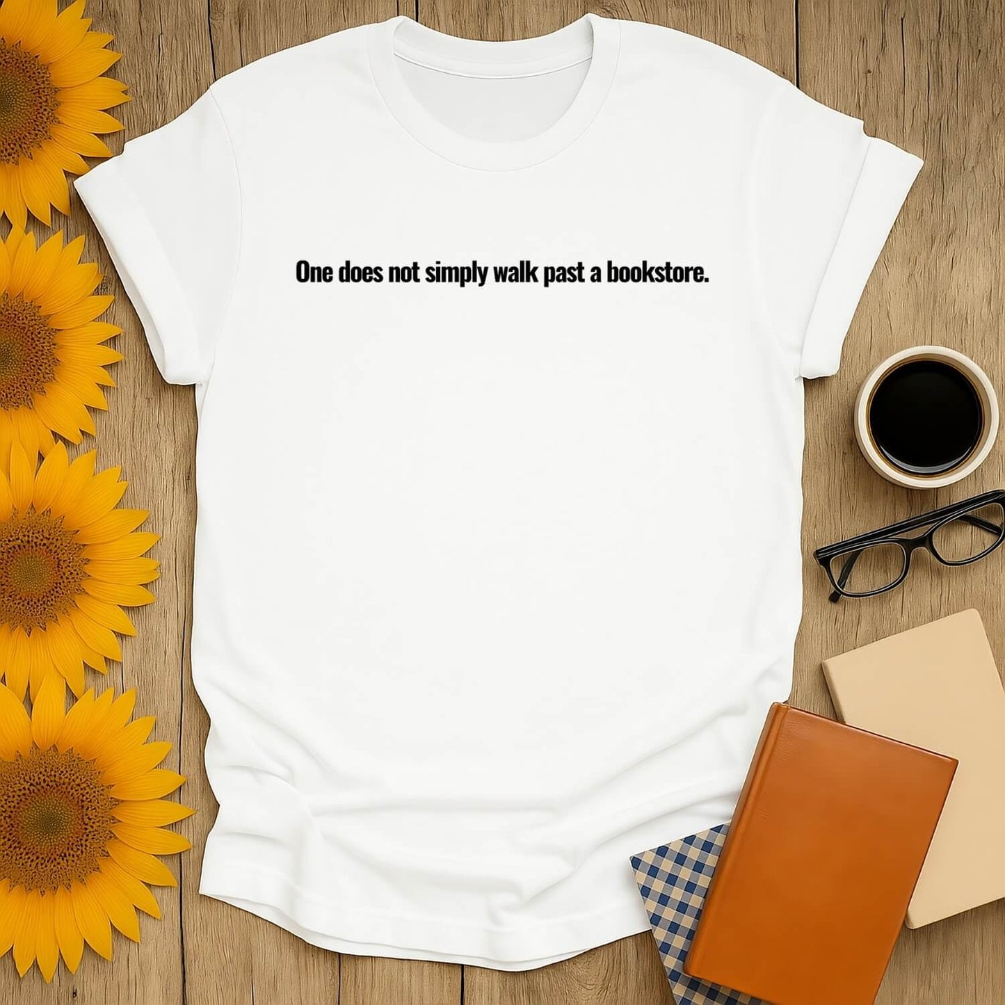 White t-shirt with text 'One does not simply walk past a bookstore' surrounded by sunflowers and books.