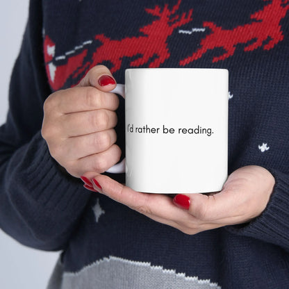 A cozy ceramic mug with the text 'I'd rather be reading' held by a person in a festive sweater, ideal for book lovers.