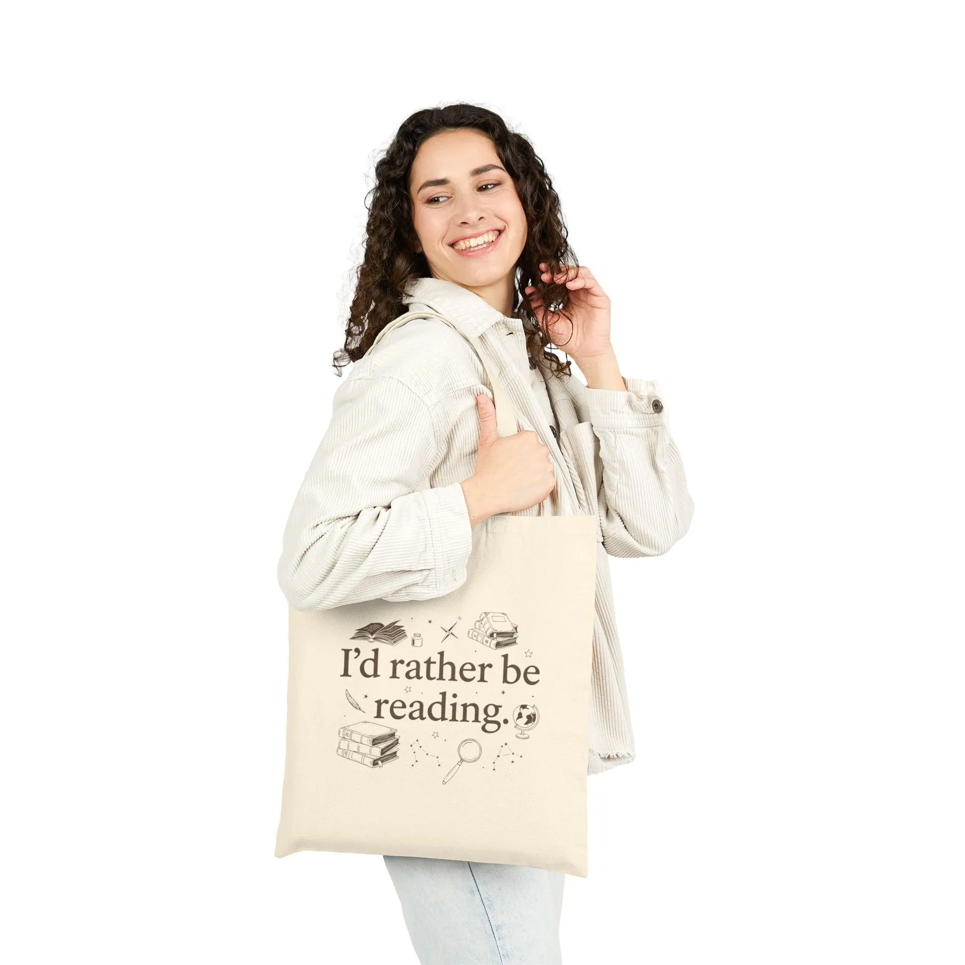 A smiling woman shows off the Rather Be Reading 2 Tote Bag with vintage book illustrations and the phrase "I'd rather be reading."