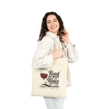 A joyful person holding the 'Read Between the Wines Tote Bag' featuring a wine glass and playful text, perfect for book lovers.