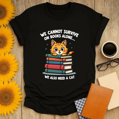 Cozy black tee featuring a cute cat atop stacked books, saying "We cannot survive on books alone... we also need a cat!" Perfect for book lovers.