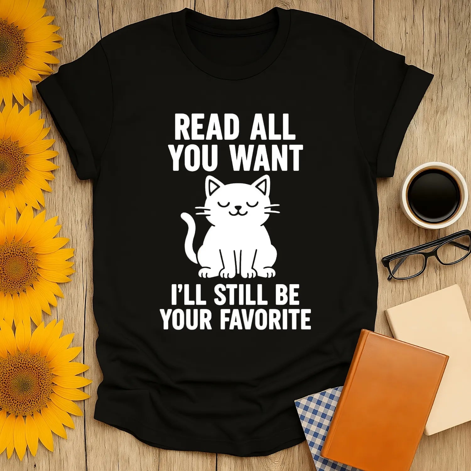 Cozy black t-shirt with a cute cat illustration and witty text: 'Read All You Want, I'll Still Be Your Favorite' for cat-loving bookworms.