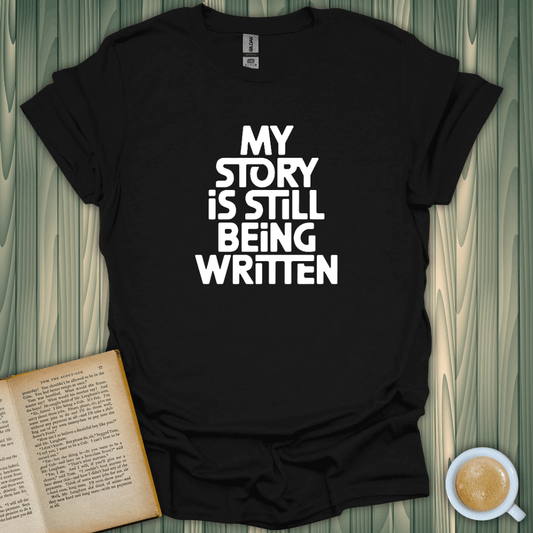 Black Story Still Writing T-Shirt for book lovers, featuring bold screen-printed text, comfy unisex fit.