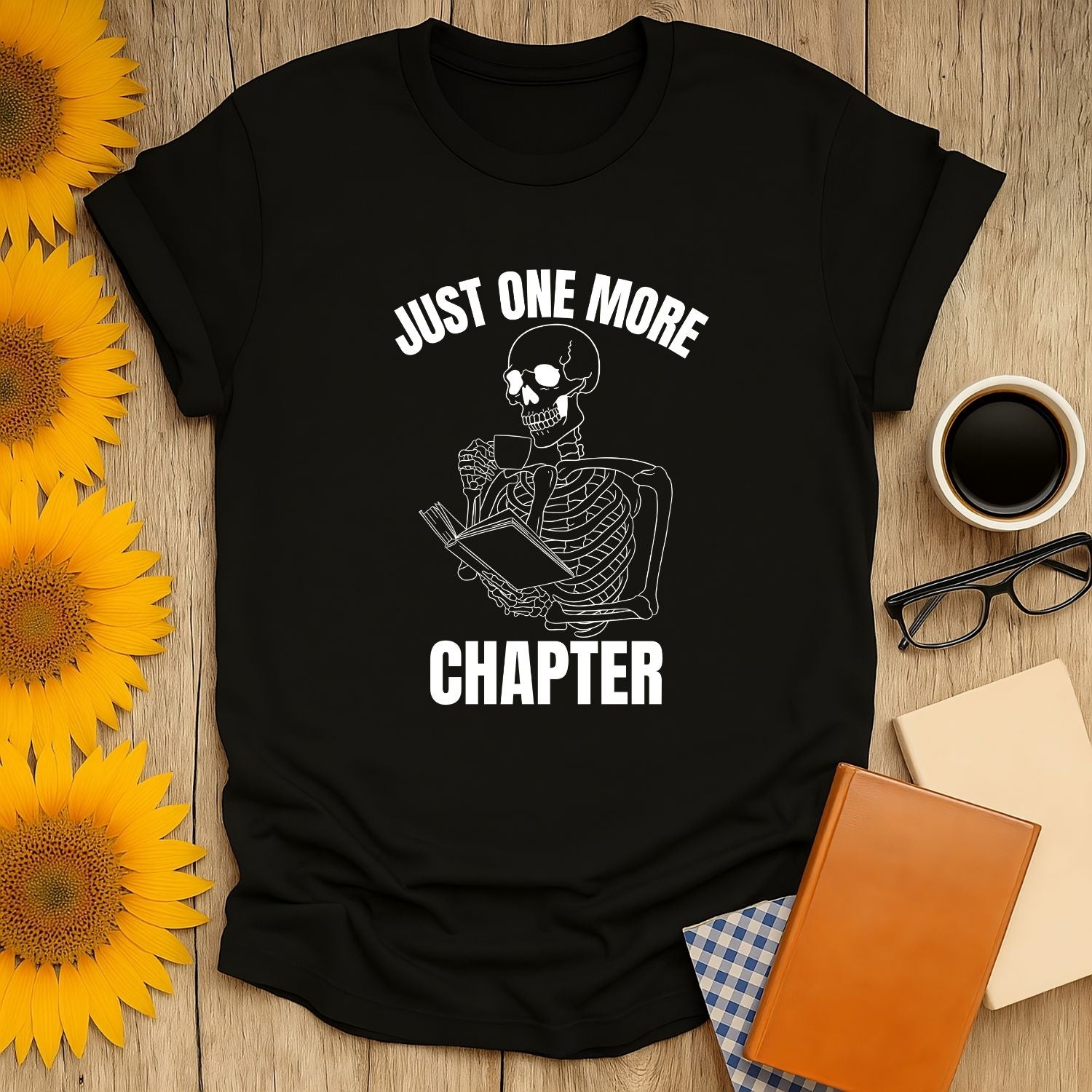 Skeleton Reader T-Shirt featuring a skeleton with a book, saying 'Just One More Chapter'—a cozy gift for book lovers.