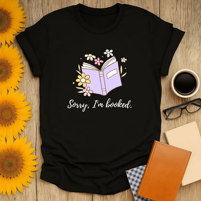 Funny book lover shirt featuring an illustrated book and flowers with the text 'Sorry, I’m booked.' Perfect for cozy reading vibes.