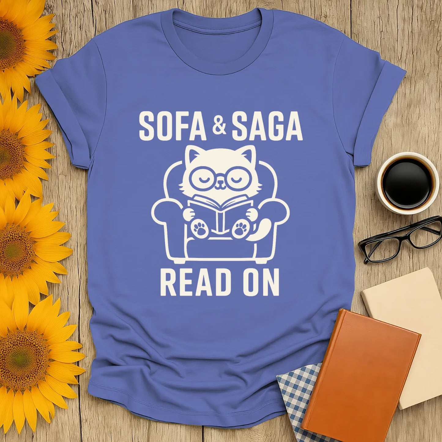 Cozy cat reading a book on a sofa. Text reads 'SOFA & SAGA READ ON'. Perfect funny reading tee for book lovers.
