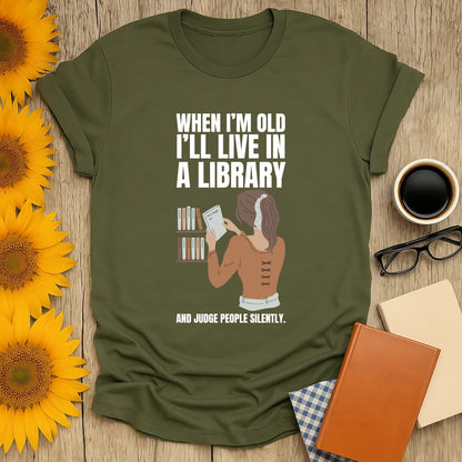 Funny reading tee with a woman in a library, text: 'When I'm old I'll live in a library and judge people silently.' Perfect gift for book lovers!