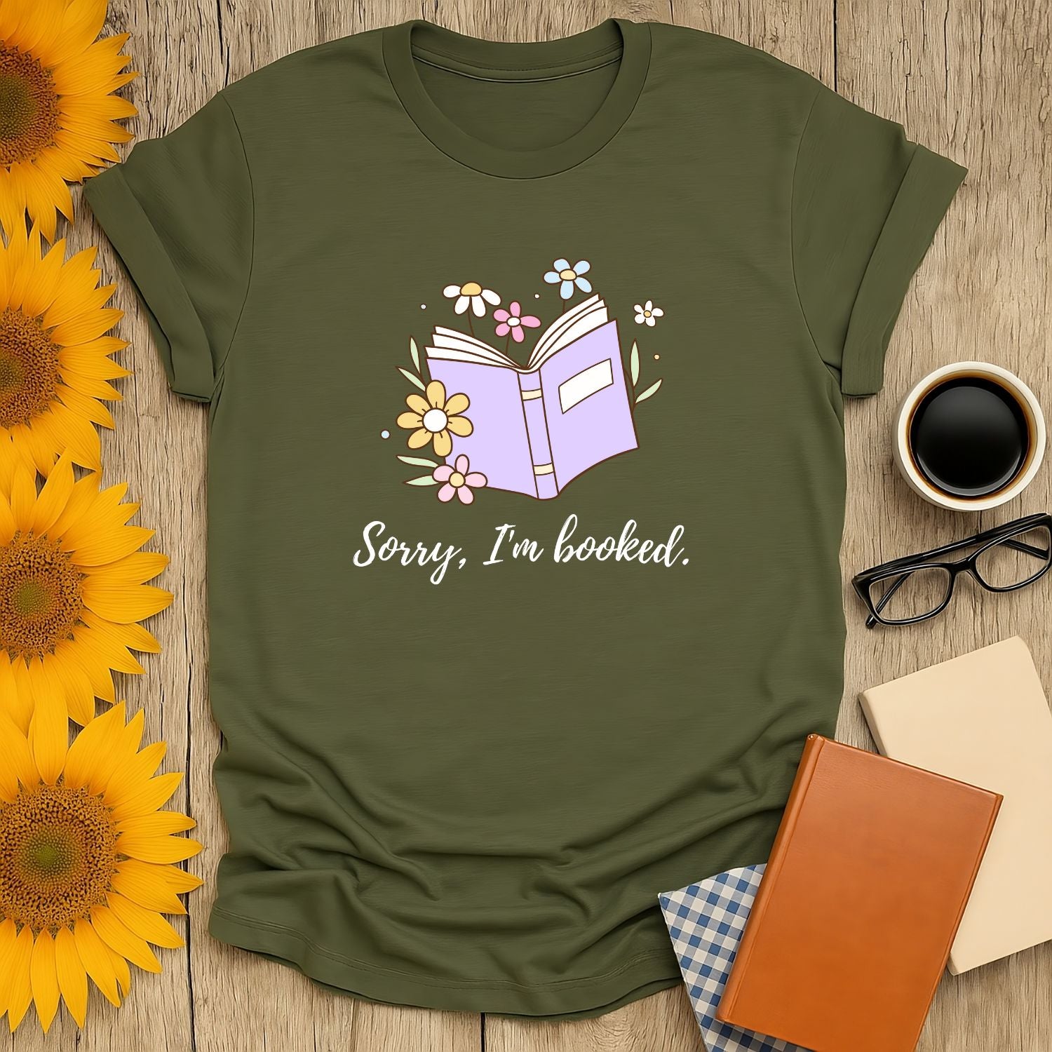 A cozy olive tee featuring an open book with flowers and the text 'Sorry, I'm booked.' Perfect for book lovers who savor cats, coffee, and tea!