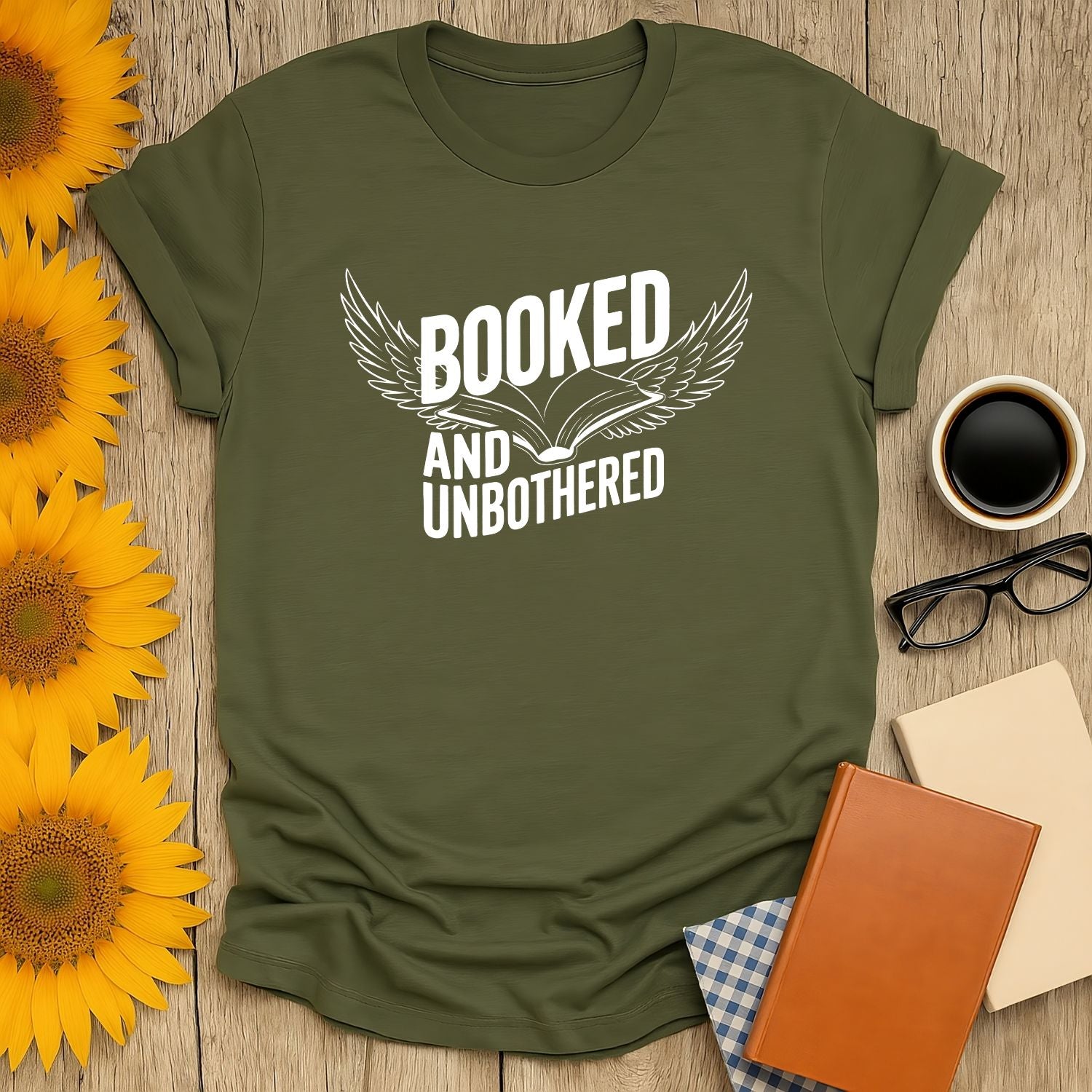 Olive green 'Booked and Unbothered' t-shirt with a book and wings design, perfect for cozy reading lovers and cat enthusiasts.
