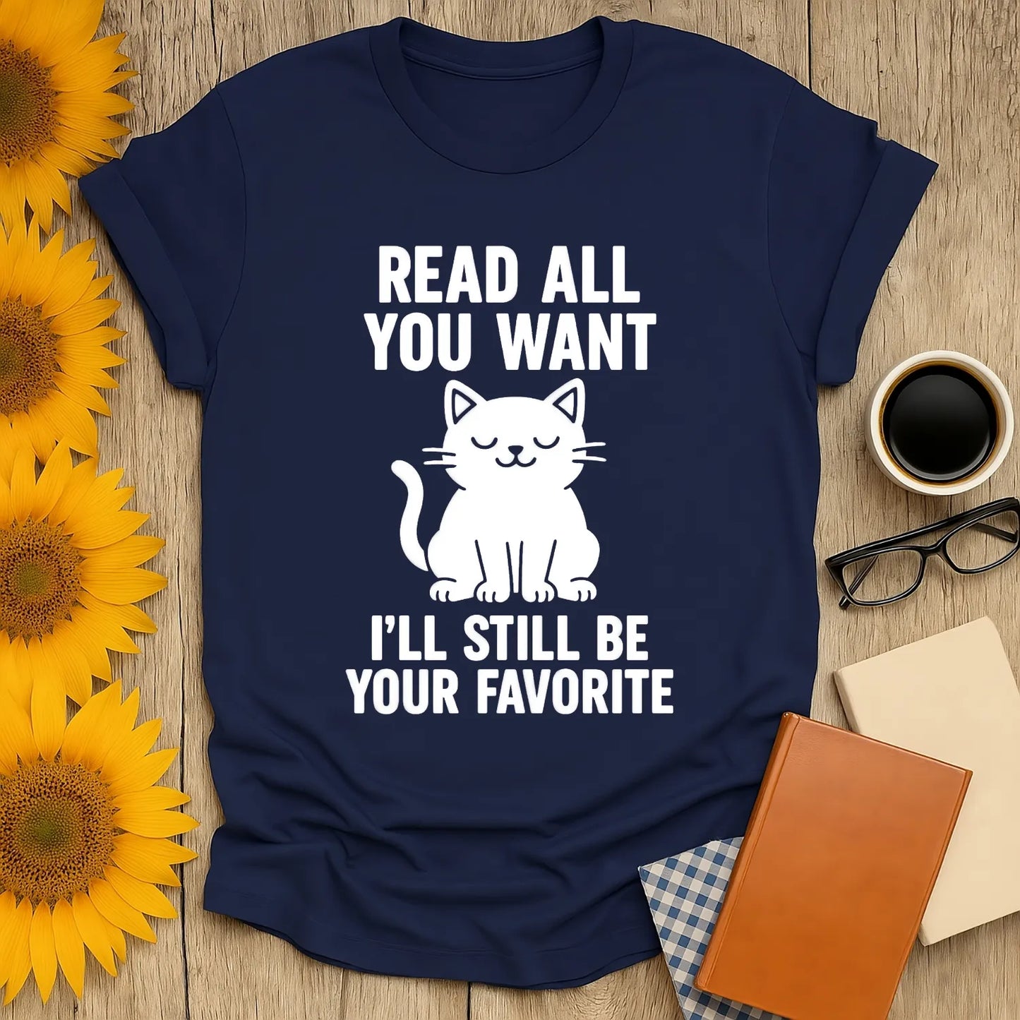 Navy t-shirt with a cute cat illustration and text 'Read All You Want, I'll Still Be Your Favorite' for book lovers.