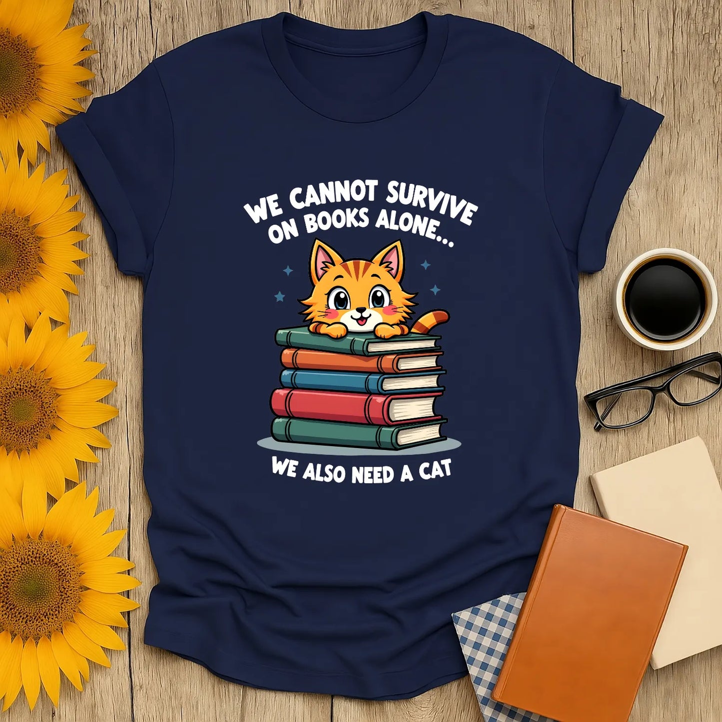 Cozy navy tee with a cute cat on stacked books and the text, "We cannot survive on books alone... We also need a cat." Perfect for book lovers!