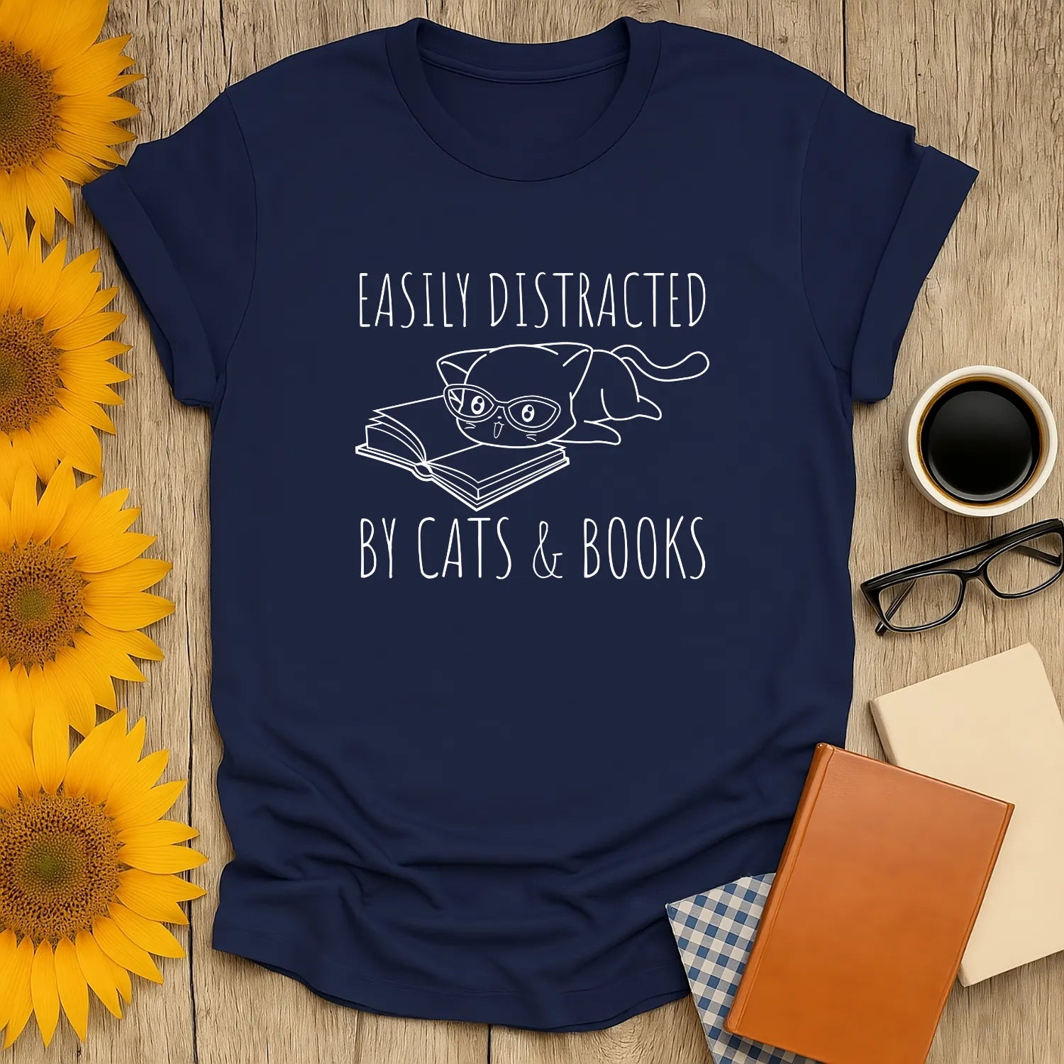 Navy t-shirt with design reading 'Easily Distracted by Cats & Books' featuring a cat in glasses over an open book. Perfect gift for book lovers.
