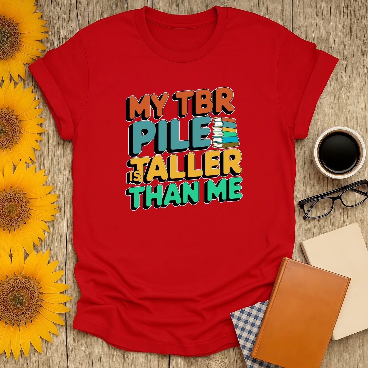 A bright red t-shirt featuring the humorous text 'My TBR Pile is Taller Than Me,' perfect for book lovers who adore cats, coffee, and cozy reads.