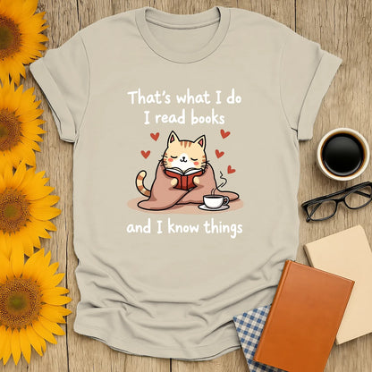 Cozy kitty reading a book with a cup, saying 'That's what I do I read books and I know things'—perfect gift for cat-loving bookworms.