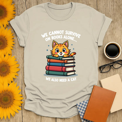 Cozy t-shirt featuring a cute cat atop stacked books with the text, 'We cannot survive on books alone… We also need a cat'.