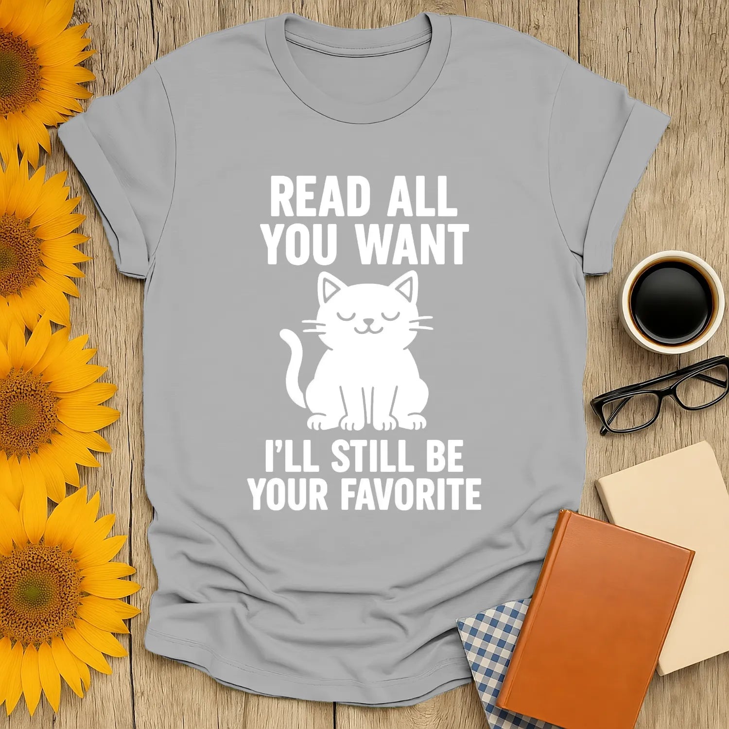 Cozy gray tee with a cute cat graphic and text: 'Read All You Want, I'll Still Be Your Favorite'—perfect for cat and book lovers.