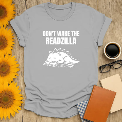 Playful gray t-shirt with a cute sleeping dinosaur on books and text 'Don't Wake the Readzilla'—perfect for cozy book lovers.