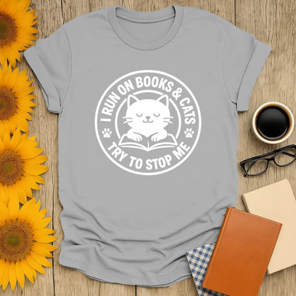 Cozy cat reading shirt with playful text: 'I Run on Books & Cats, Try to Stop Me'—perfect gift for book lovers and cat enthusiasts.