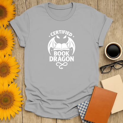 Light gray t-shirt with "Certified Book Dragon" and dragon design; ideal gift for book lovers, cats, coffee, or tea enthusiasts.