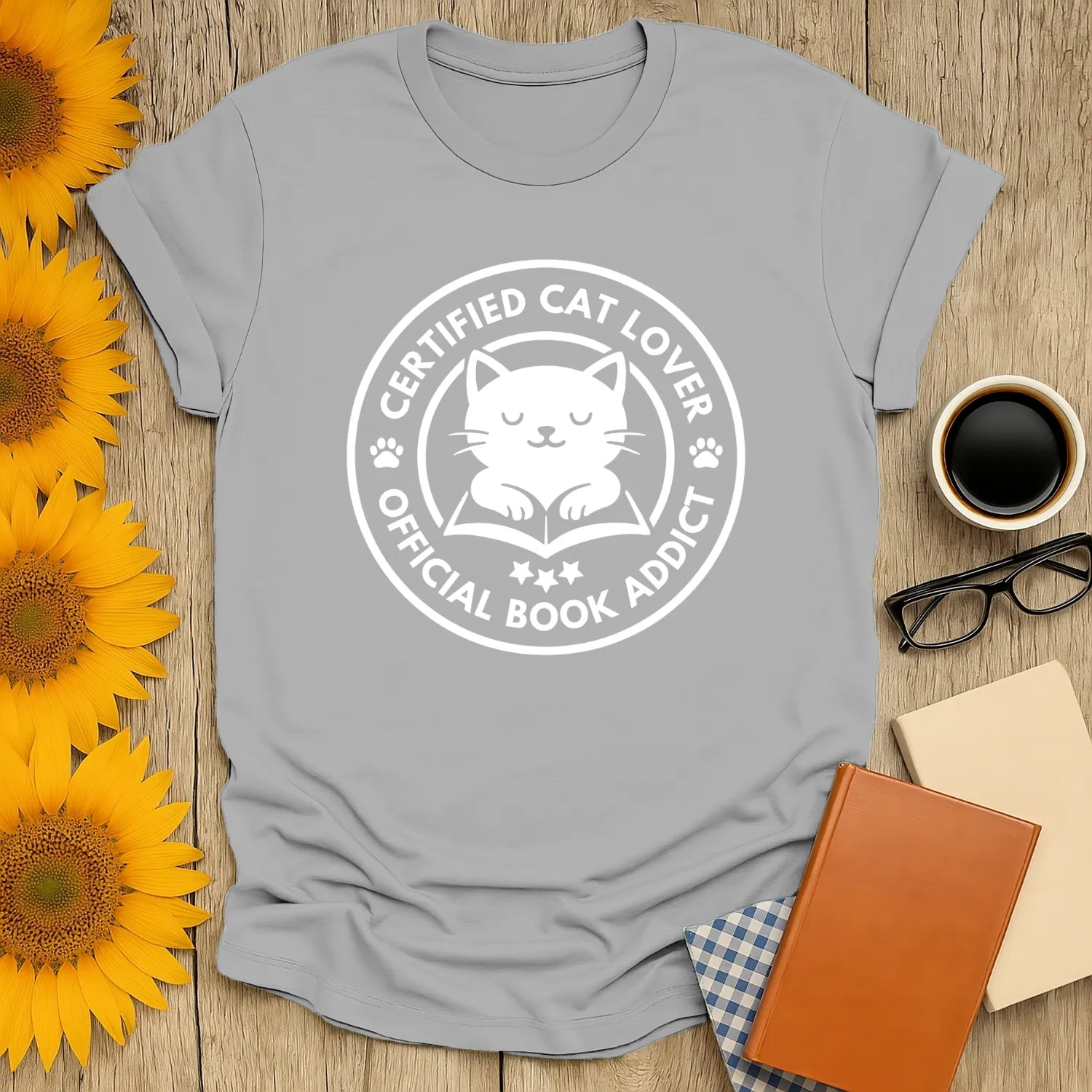 A cozy gray t-shirt featuring a cute cat illustration and text saying 'Certified Cat Lover, Official Book Addict'.