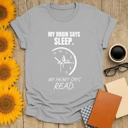Funny book lover shirt featuring a clock illustration with text: 'My brain says sleep. My heart says read.' Perfect for cozy nights!