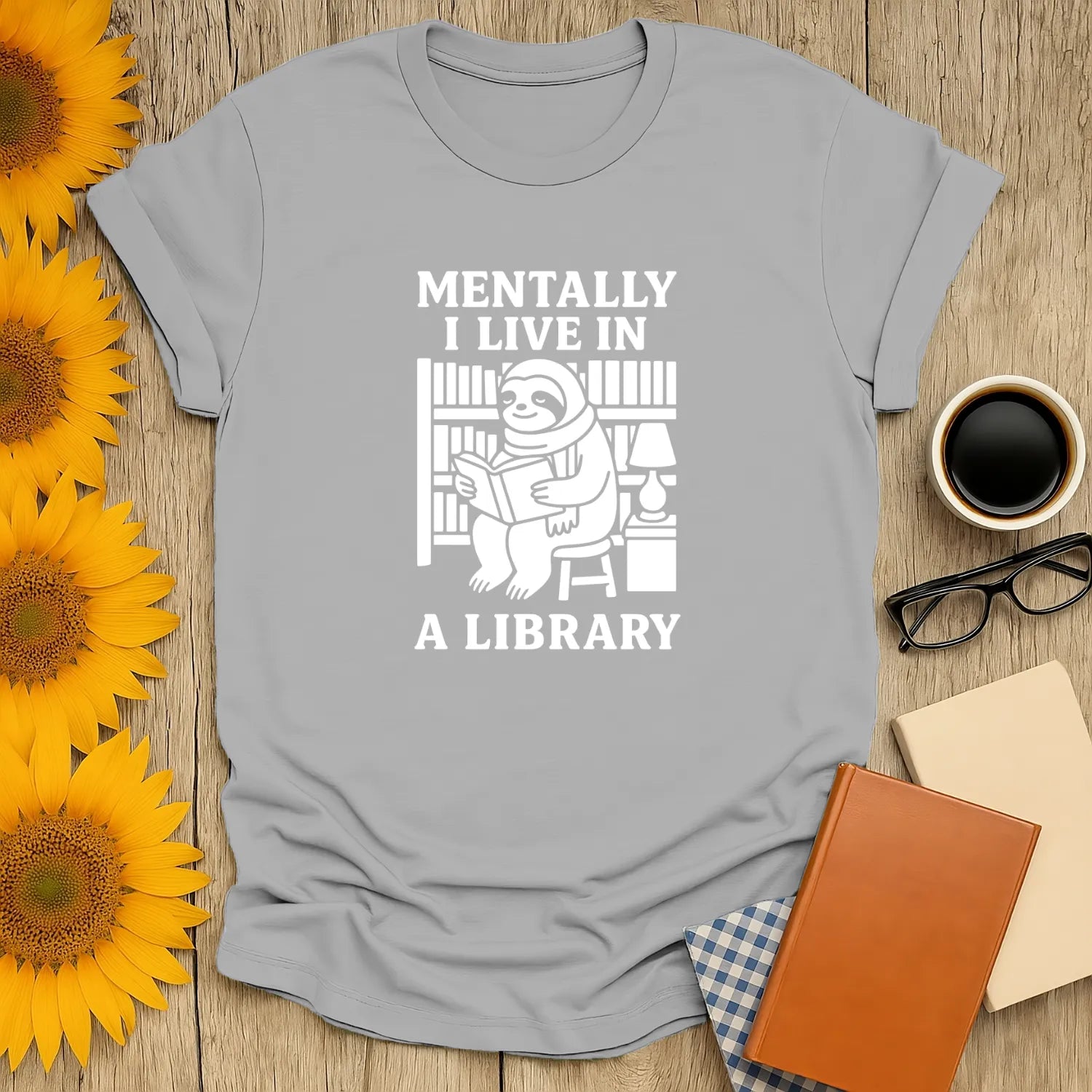 Light gray t-shirt featuring a sloth reading among shelves, with the text 'Mentally I Live In A Library.' Perfect gift for book lovers.