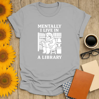 Light gray t-shirt featuring a sloth reading among shelves, with the text 'Mentally I Live In A Library.' Perfect gift for book lovers.