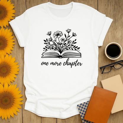 Cozy book lover shirt with blooming flowers above an open book and whimsical text: 'one more chapter'.